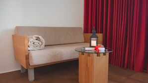 Una habitación con un sofá, una mesa de centro de vidrio, una cortina roja y una vela encendida.