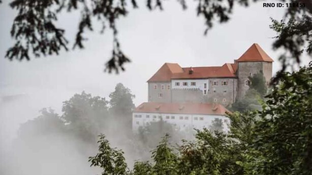 Un edificio de estilo castillo con techo rojo, rodeado de árboles y niebla.