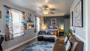 Ein Schlafzimmer mit Bett, Deckenventilator, Schreibtisch, Stuhl, einer Couch und Kunstwerken an den Wänden.