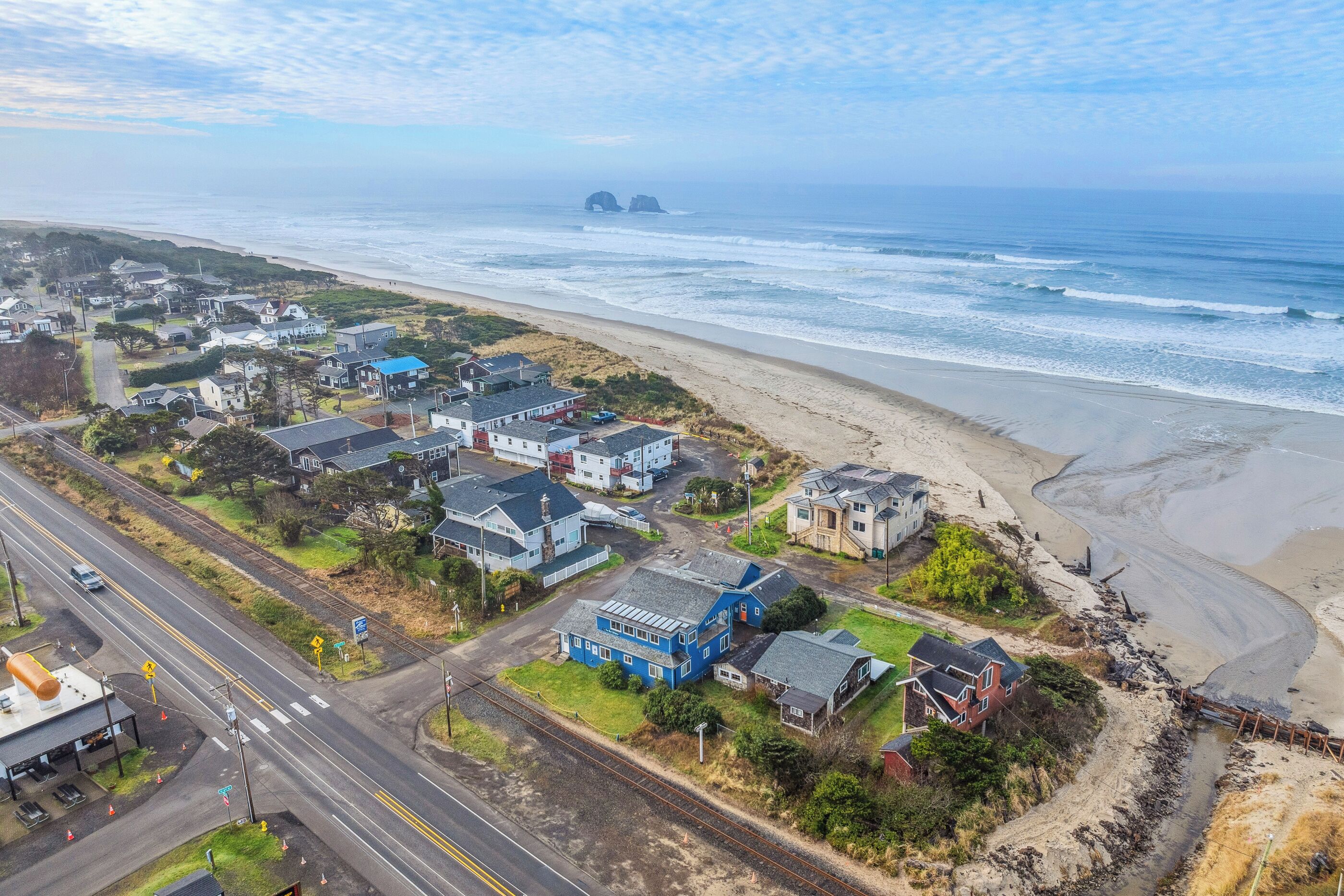 An aerial view of a coastal town with houses near the beach, a road, and a railway track.