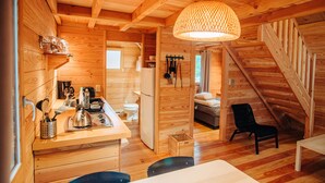 A cozy wooden cabin with a kitchen area, a dining table, and a staircase leading to a loft bed. - Chalets Huttopia White Mountains (Conway)