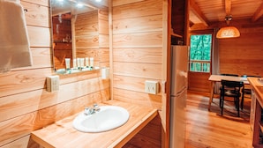 A wooden cabin interior with a wooden sink, mirror, and a dining area with a table and chairs. - Chalets Huttopia White Mountains (Conway)