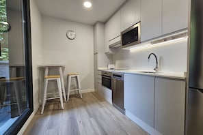 Une cuisine moderne avec des meubles blancs, des appareils en acier inoxydable, un four à micro-ondes et une horloge au mur.