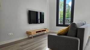 Ein modernes Wohnzimmer mit einem grauen Sofa, einer Holz-Unterhaltungsecke und einem großen Fenster mit Balkonblick.