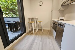 Una cocina moderna con un amplio ventanal, taburetes blancos, un reloj y electrodomésticos de acero inoxidable.