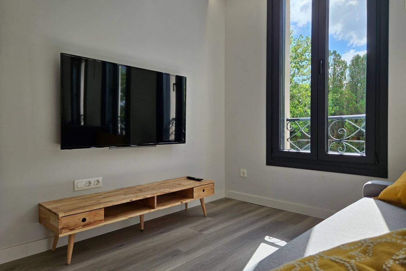 A modern room with a large TV mounted on the wall, a wooden bench, and a window with a balcony view.