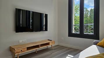 A modern room with a large TV mounted on the wall, a wooden bench, and a window with a balcony view.