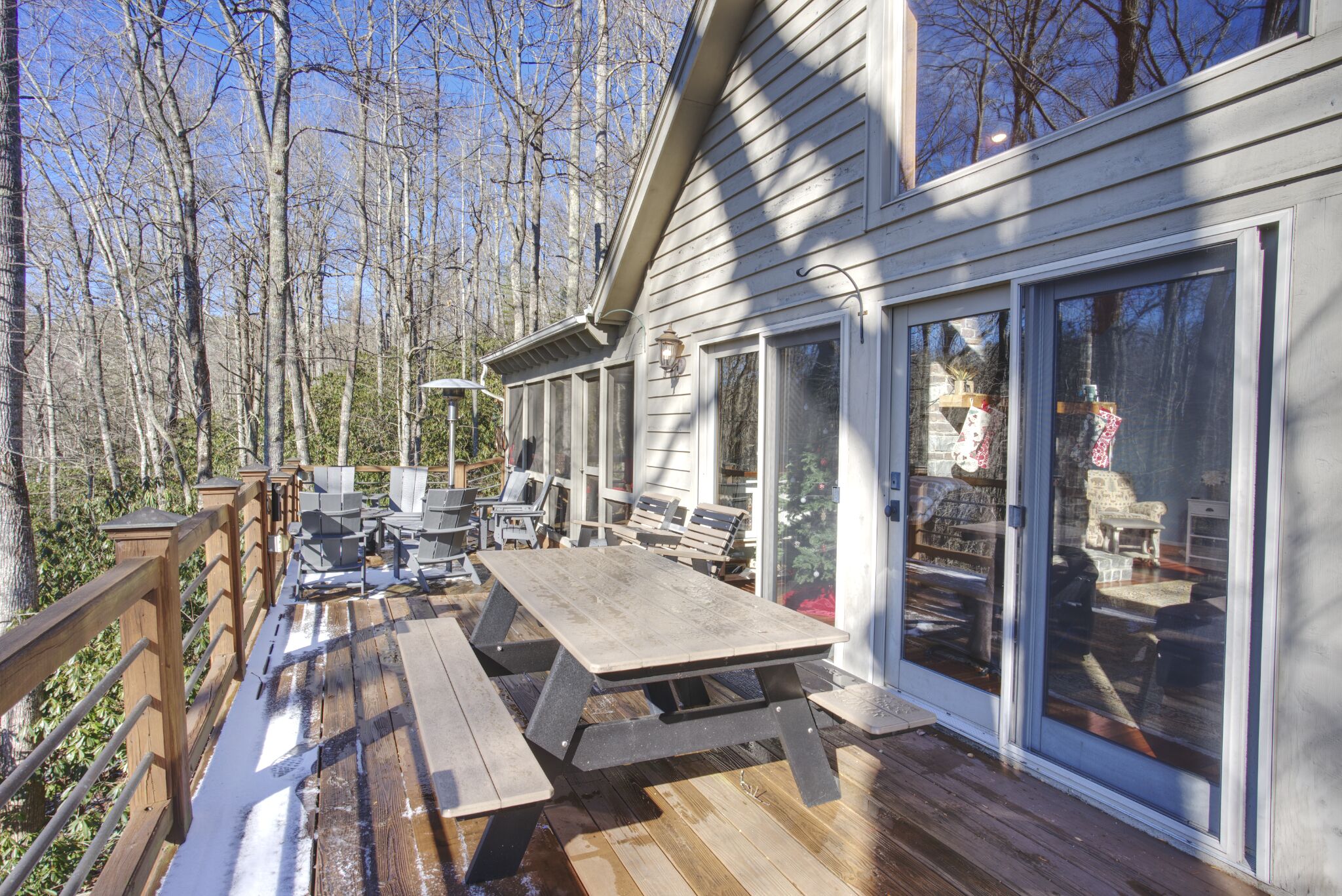 A wooden deck with picnic tables and chairs, surrounded by glass doors leading to an interior with various seating and a fireplace.
