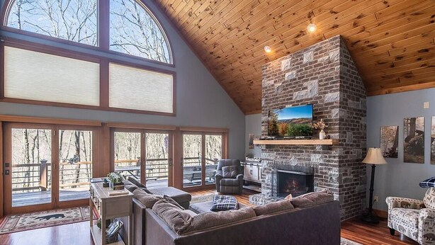 Ein geräumiges Wohnzimmer mit Kamin aus Stein, großen Fenstern und Holzboden.