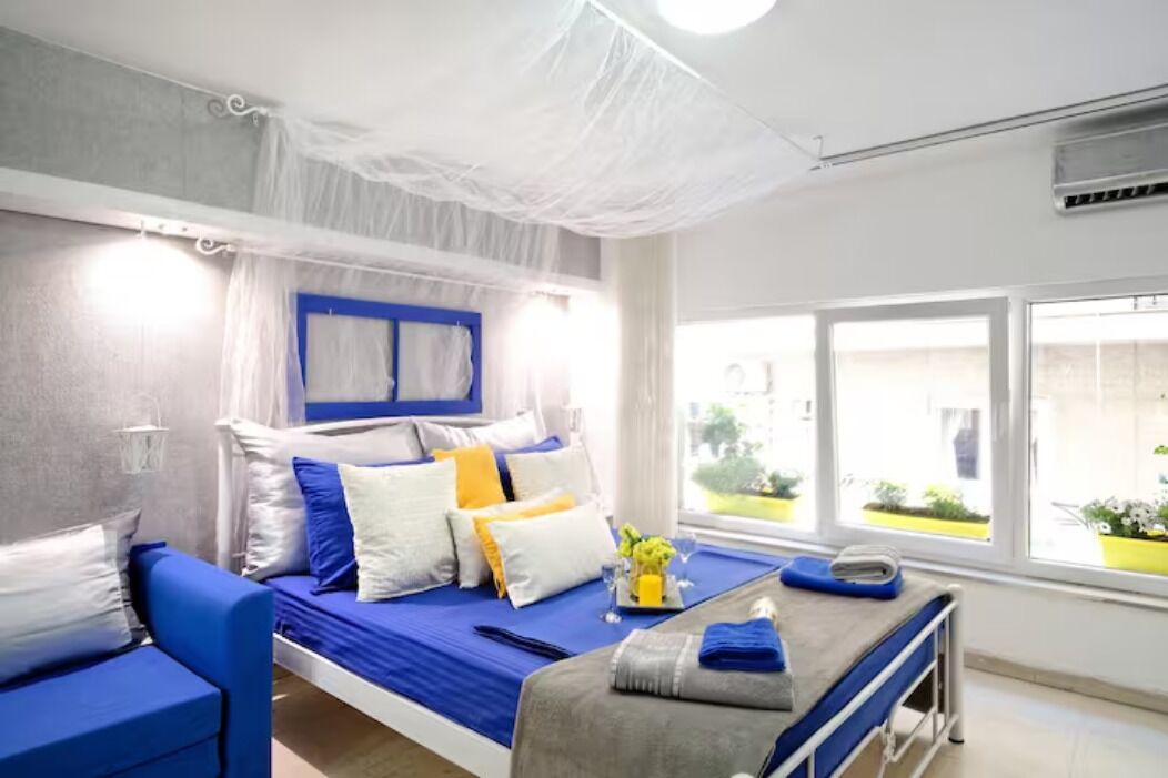 Una habitación de hotel moderna con una cama, un sofá azul y un ventanal con vistas a zonas verdes.