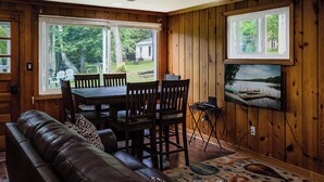 A cozy room with a wooden interior, a dining table with chairs, a leather sofa, and a television mounted on the wall. - Elemental Resort (Gwinn)