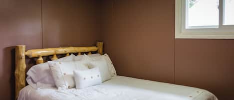 A neatly made bed with a wooden headboard and white bedding in a room with brown walls and a window.