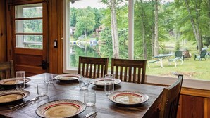 A dining table set with plates, glasses, and cutlery, with a view of a wooded area and houses through a large window. - Elemental Resort (Gwinn)