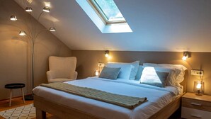 A bedroom with a skylight, a bed with pillows, bedside lamps, and a small bedside table.