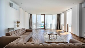 Amplia sala de estar con un sofá grande, una mesa de centro y vistas a una piscina y follaje exterior.