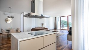 Una cocina moderna con una isla central, un comedor con una mesa redonda y una sala de estar con sofá y vistas al exterior.