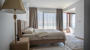 Un dormitorio moderno con una cama grande, una lámpara de noche, una mesita de noche y vistas al exterior a través de un amplio ventanal.