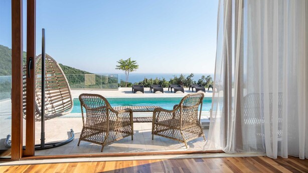 A room with a large sliding glass door leading to a pool area with wicker chairs and a view of the ocean. - Villa Beta with Pool (Budva)