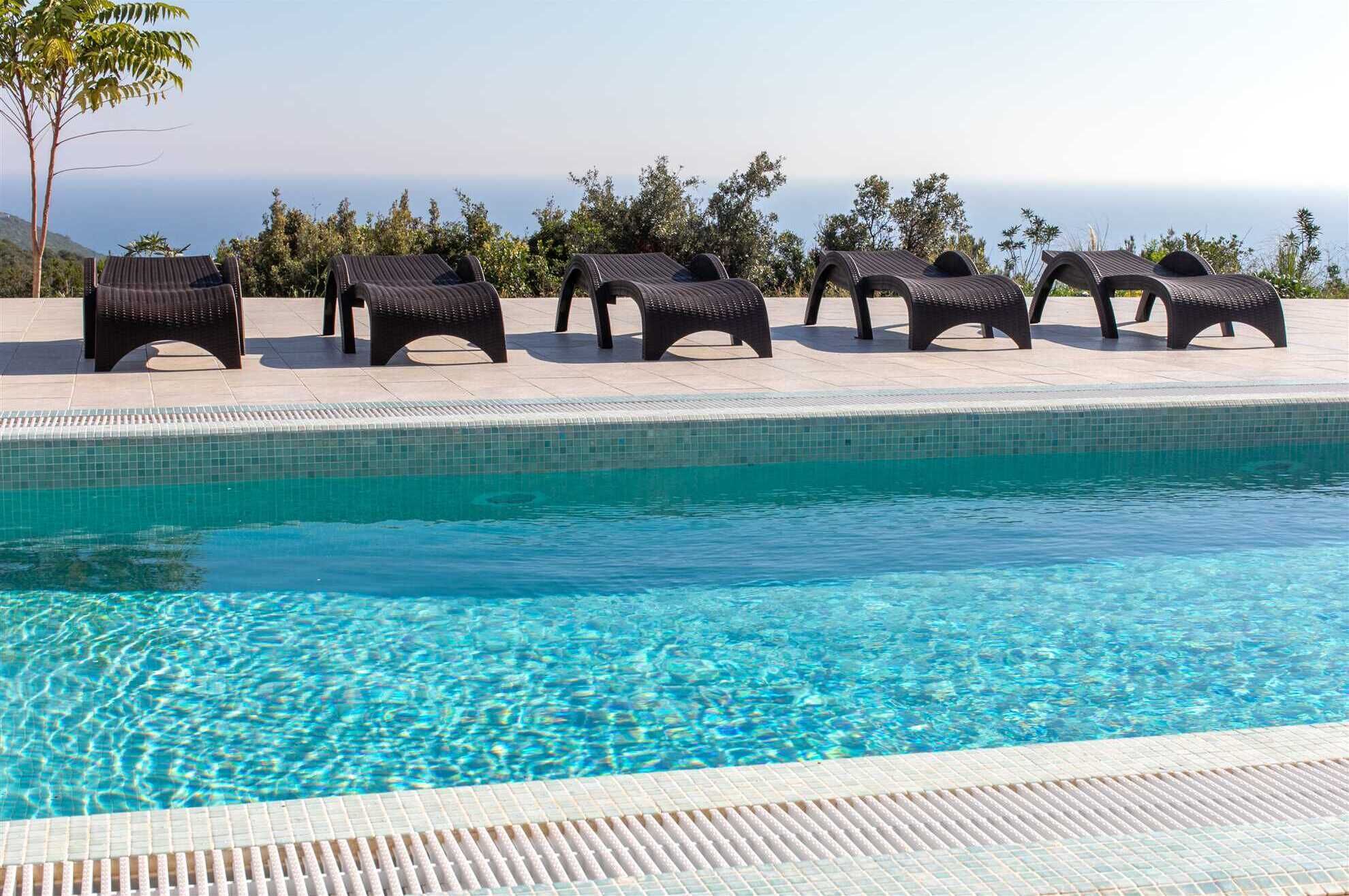 A pool with clear blue water, surrounded by lounge chairs and a tiled deck.