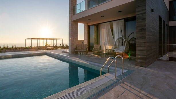 A modern poolside area with a clear view of the sunset, a glass balustrade, and a seating area with wicker chairs. - Villa Gama with Pool (Unknown)