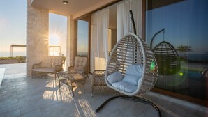 A modern outdoor seating area with wicker furniture, a hanging chair, and a view of the ocean. - Villa Gama with Pool (Unknown)
