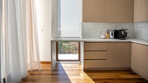 A modern kitchen with a large window, wooden flooring, and a coffee machine on the counter.