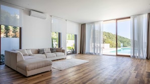 A spacious living room with a beige sectional sofa, wooden flooring, and large sliding glass doors leading to a pool.