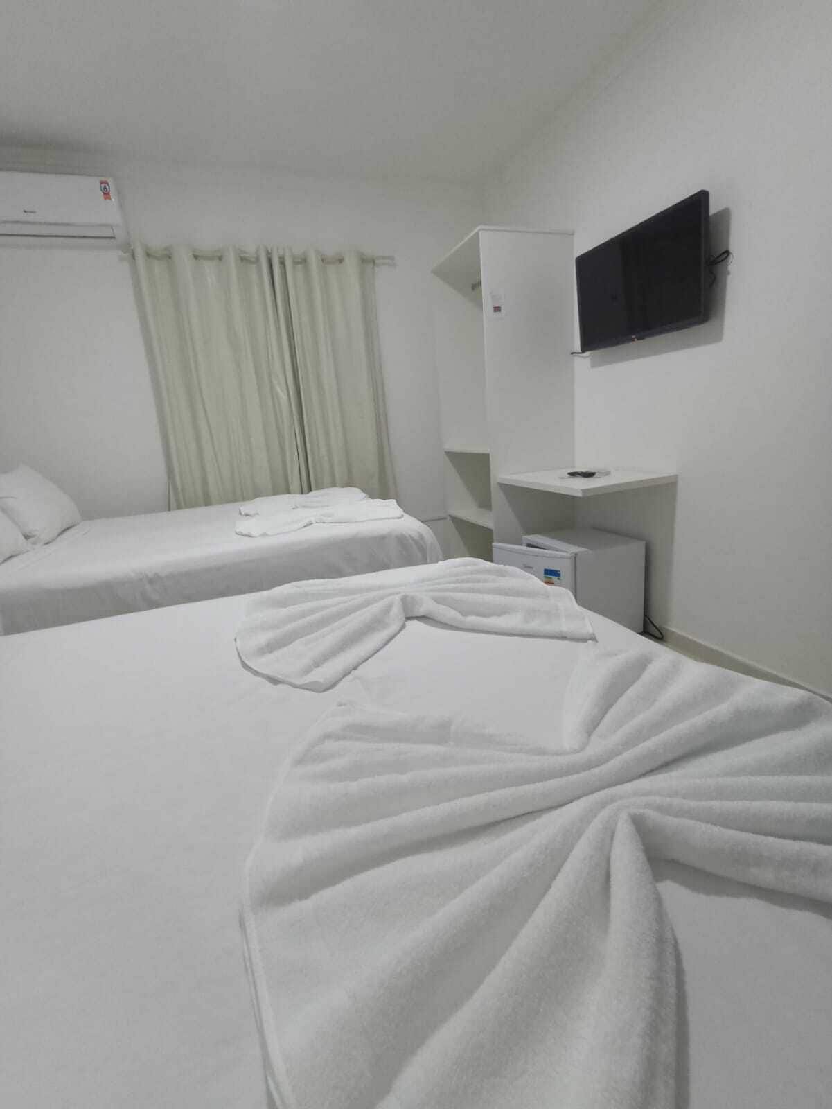 Habitación de hotel con dos camas, un televisor montado en la pared y una mesita con un control remoto.
