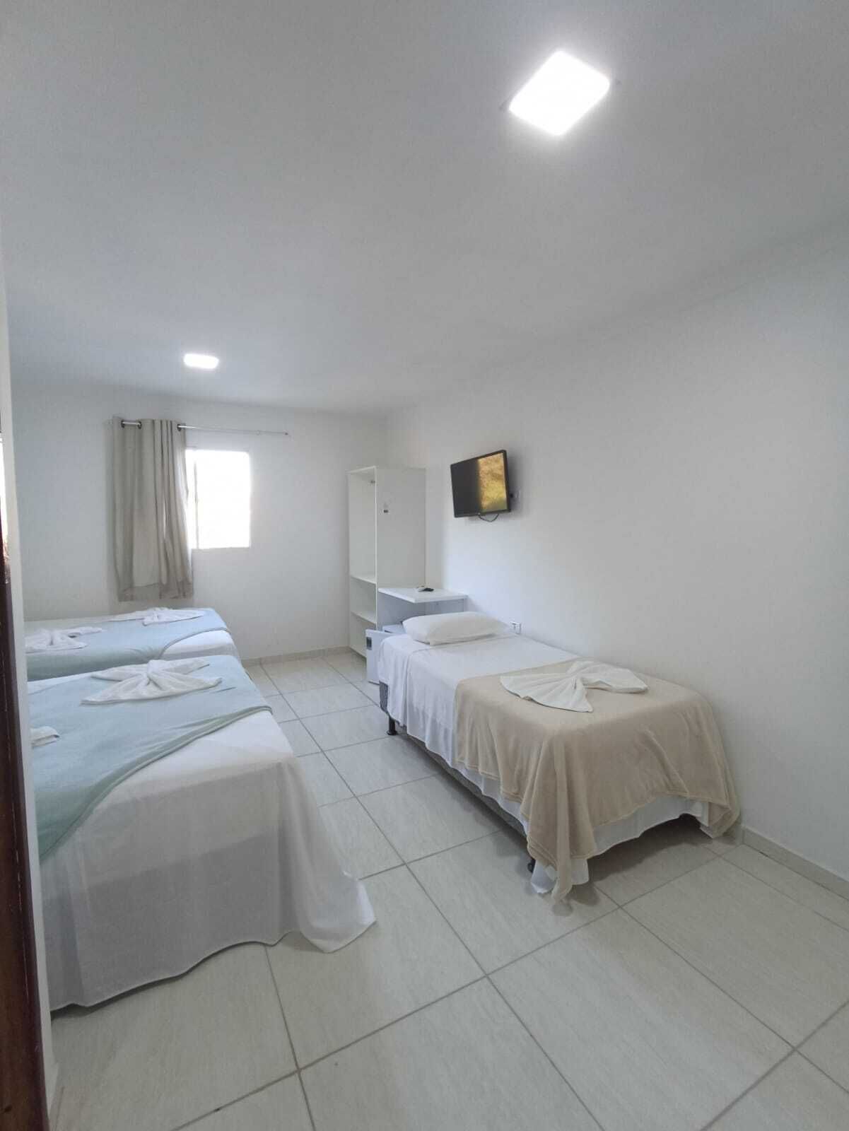 A clean, well-lit room with two single beds, a small desk, and a television on the wall.