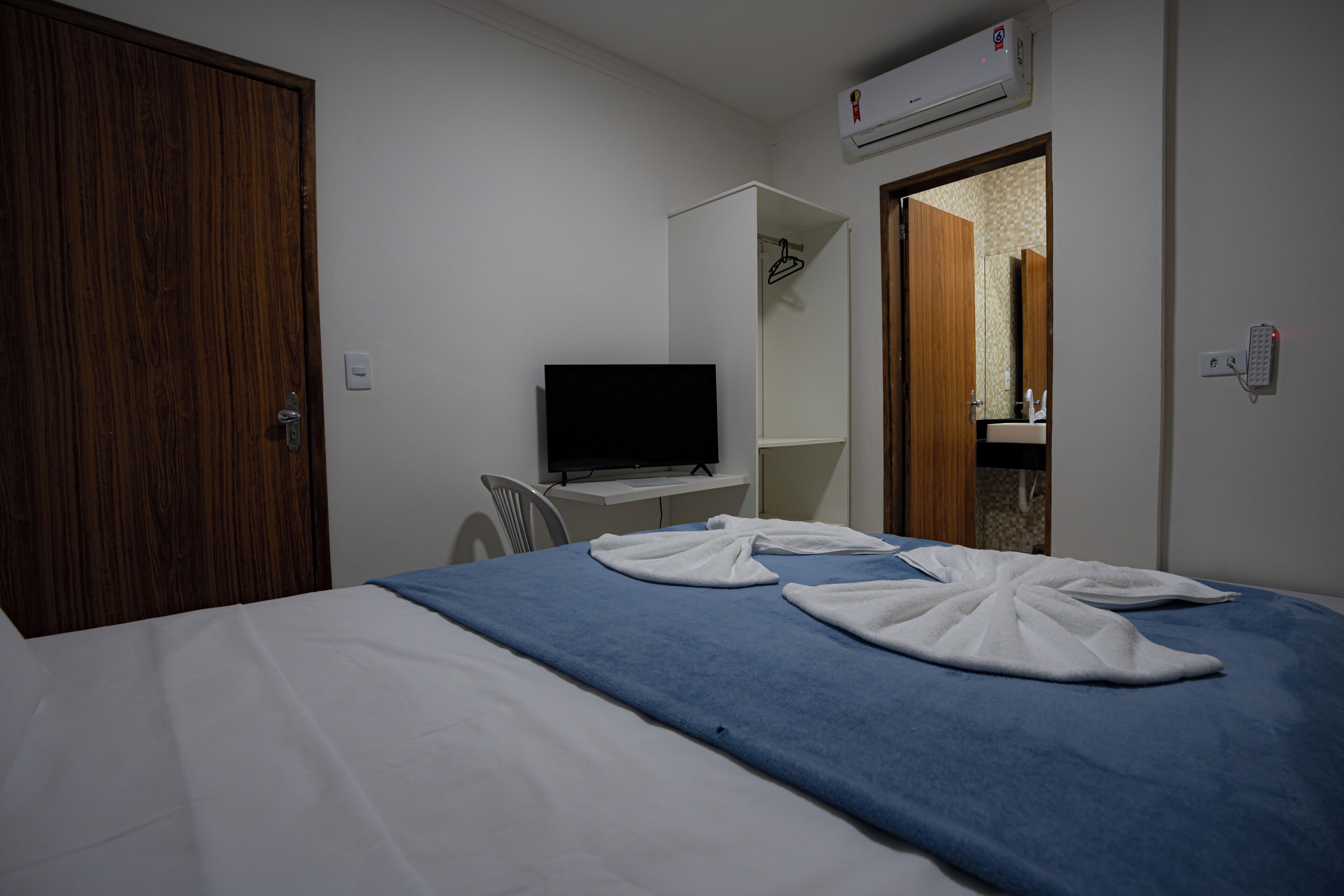 Une chambre d’hôtel avec un lit, une télévision, une armoire et une salle de bain visible à travers une porte ouverte.