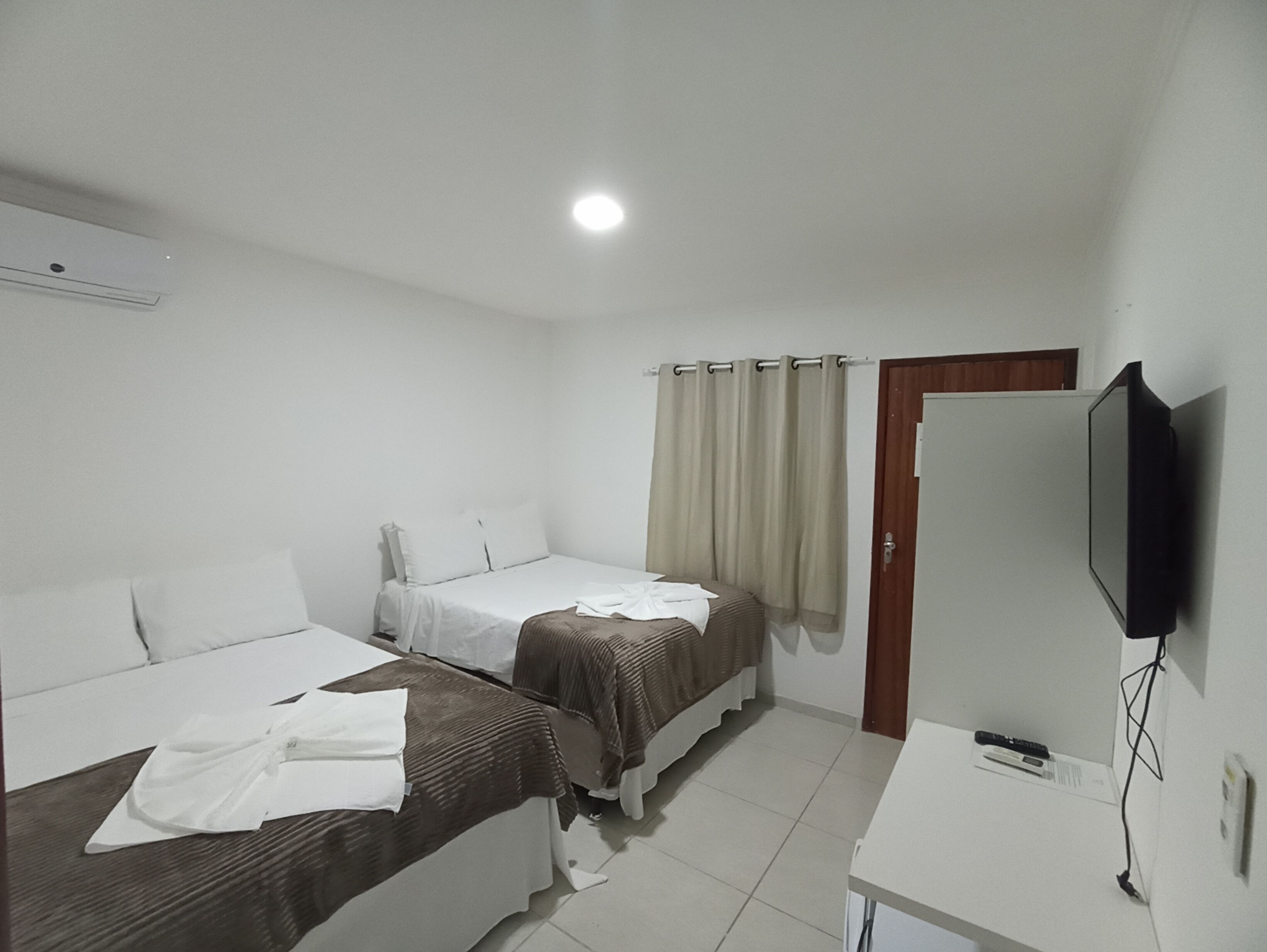 Una habitación de hotel con dos camas individuales, televisión, escritorio y puerta.