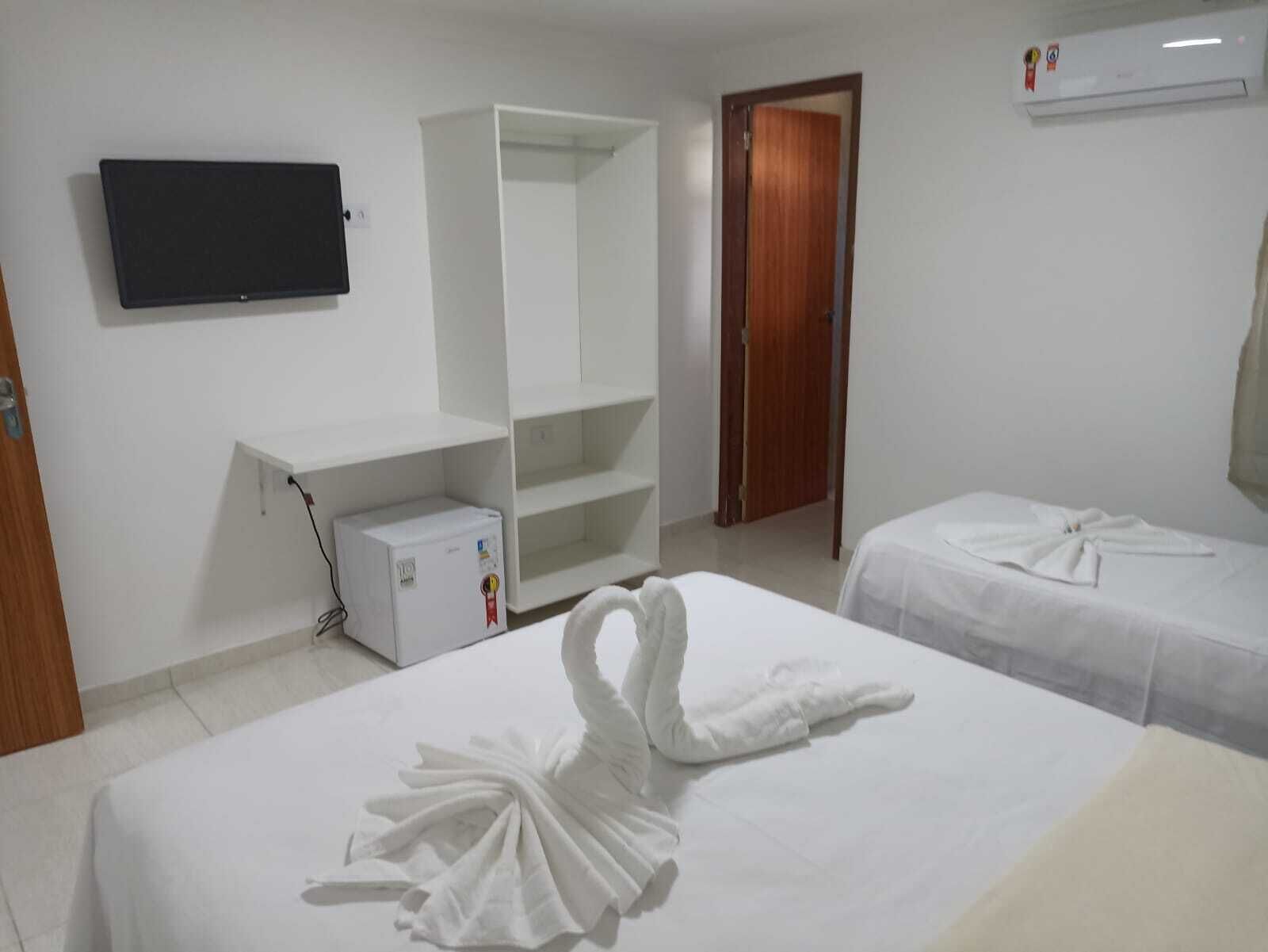 Ett hotellrum med två sängar, en tv som är monterad på väggen, en garderob och ett litet kylskåp.