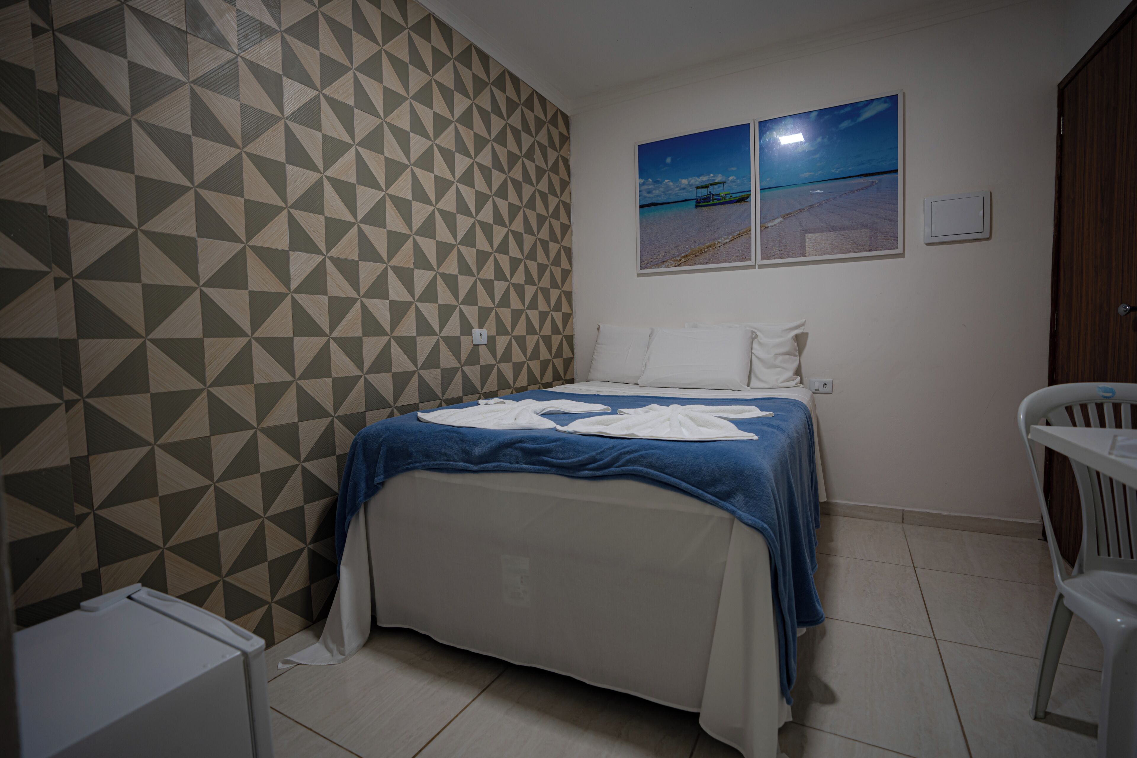 Une chambre avec un mur à motifs, un lit recouvert d’une couverture bleue, une chaise blanche et une vue sur le ciel nocturne.