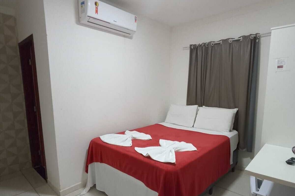 A small, clean room with a bed, a desk, and an air conditioning unit.