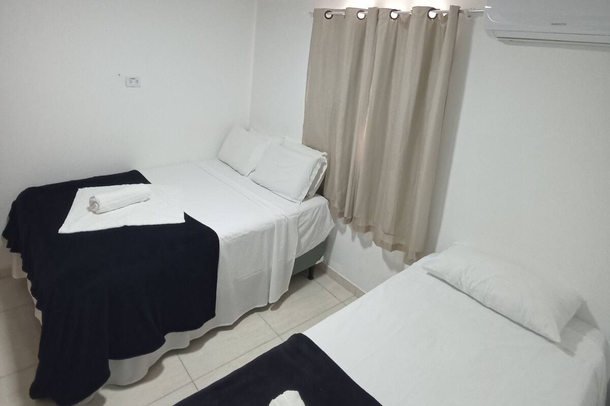 A hotel room with two beds, a ceiling light, an air conditioning unit, and a curtain.