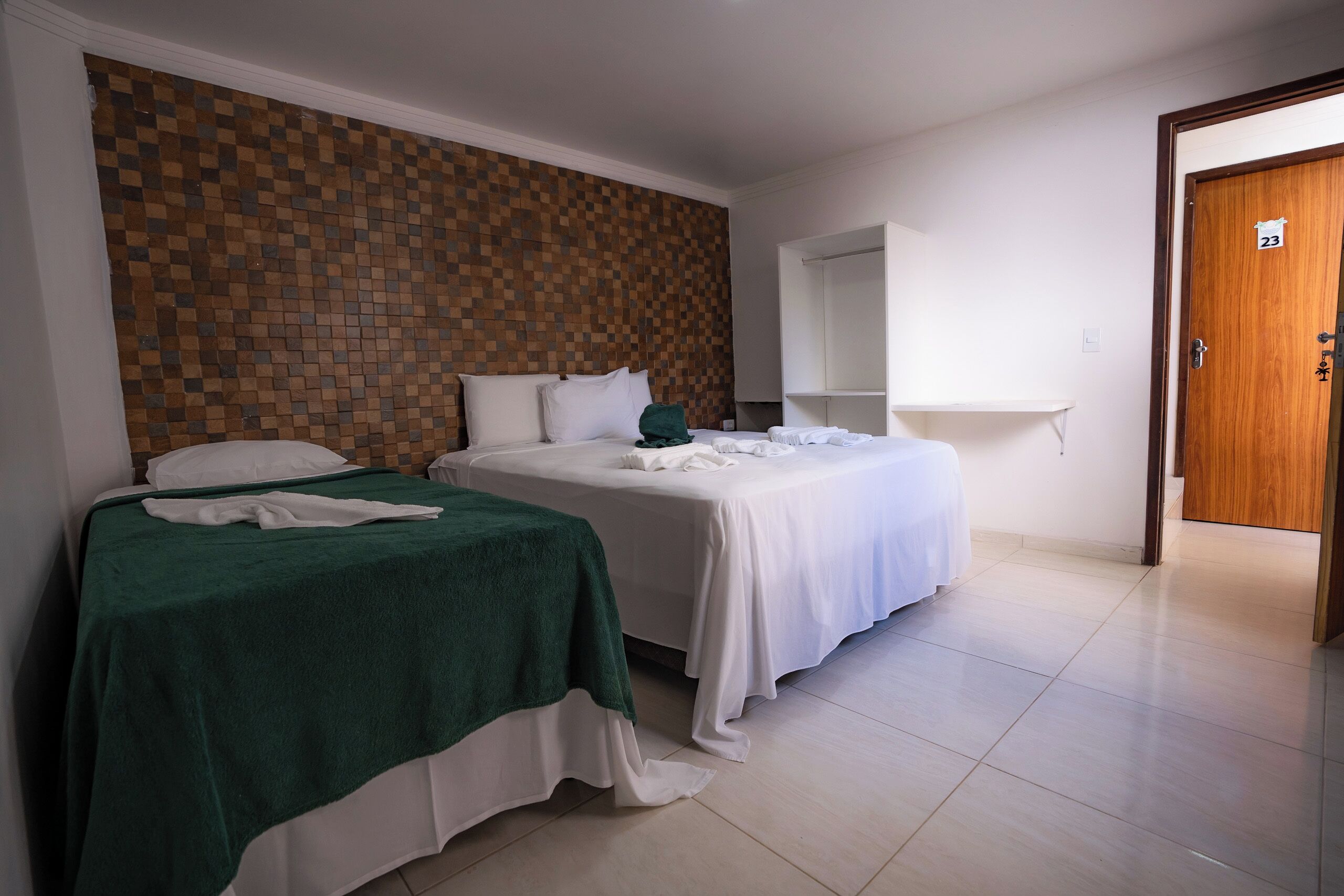 Een hotelkamer met twee bedden, een geruit wandpaneel, een houten deur en een witte kast.