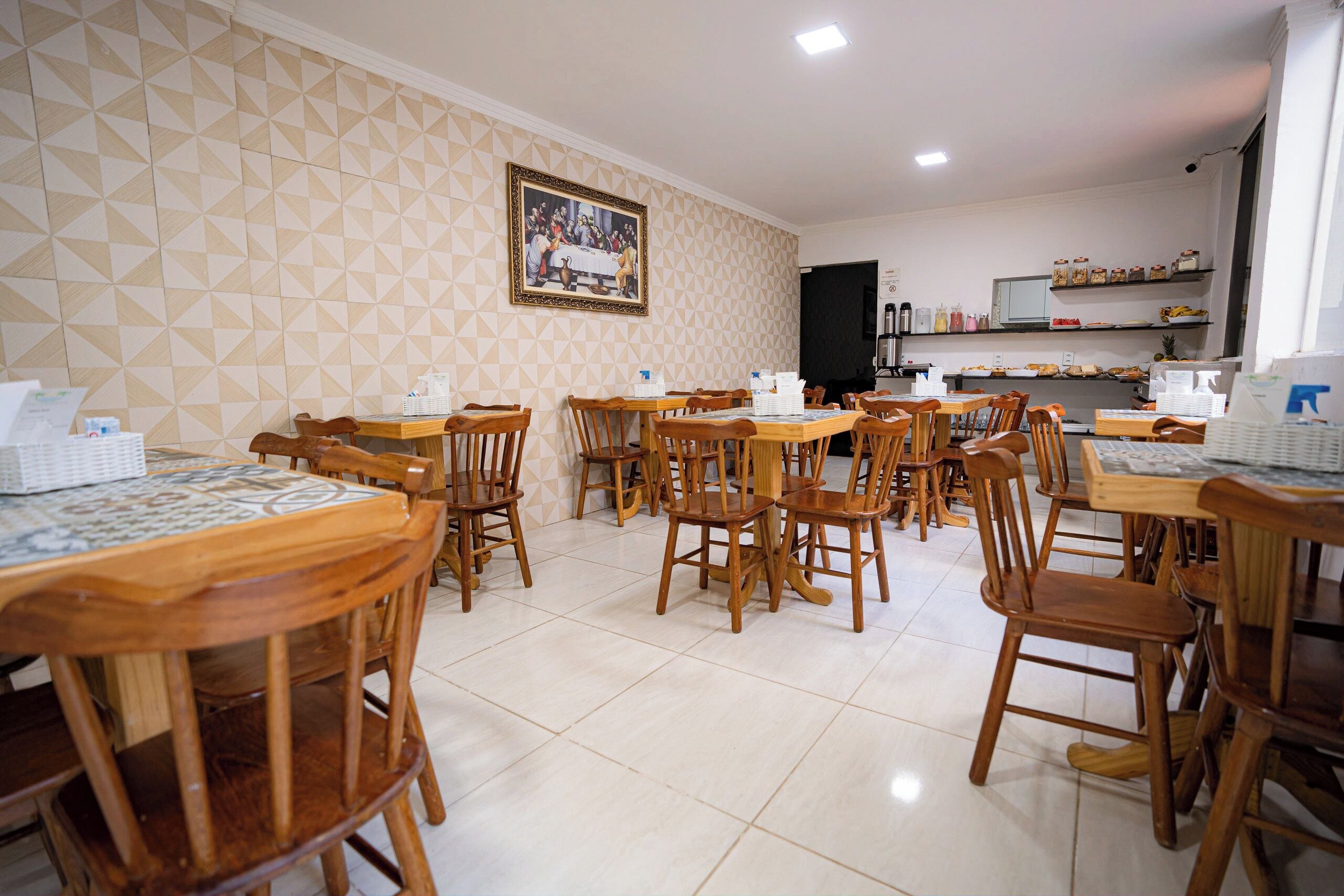 Un comedor con varias mesas y sillas de madera, suelo de baldosas y una pared con diseños geométricos.
