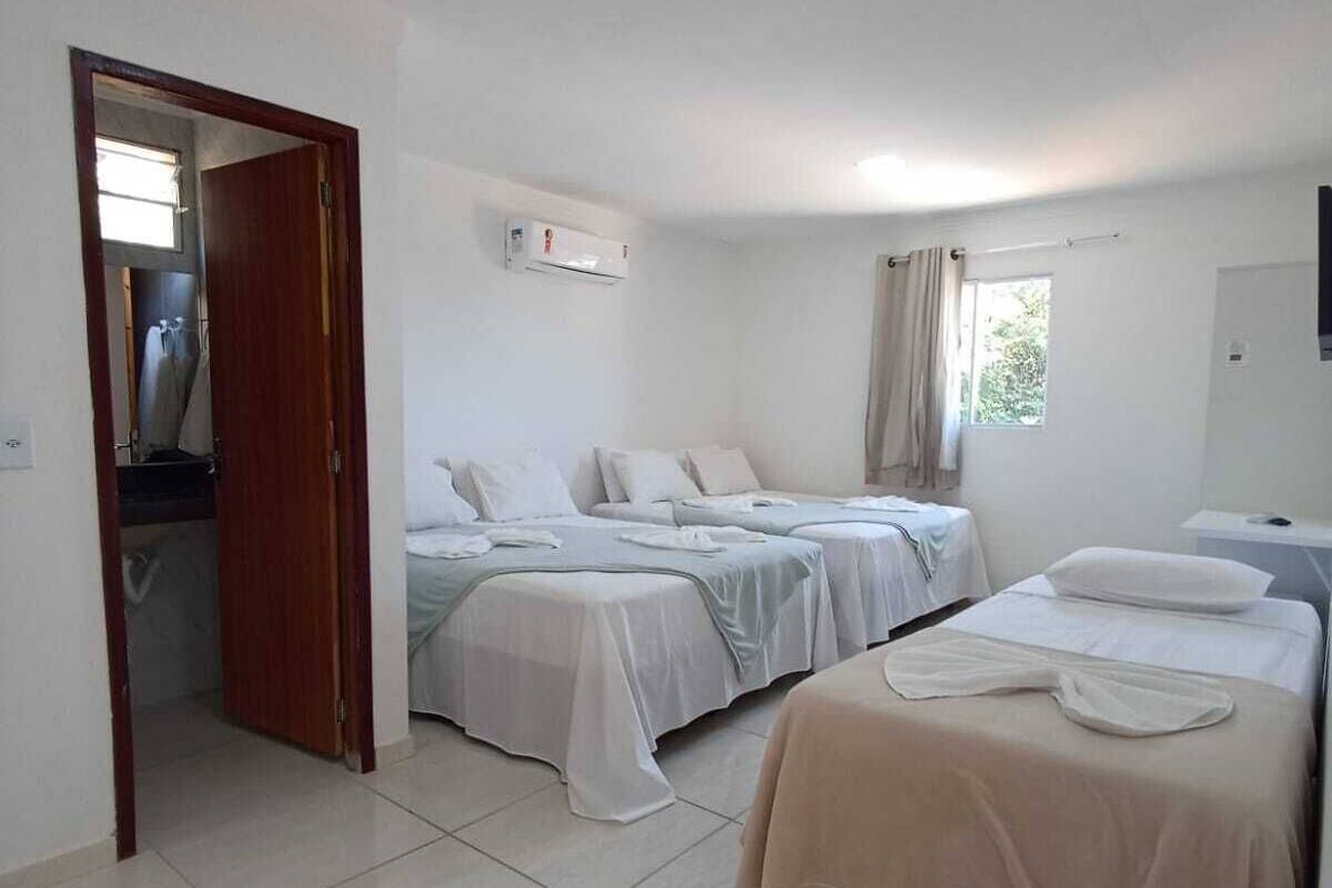 A clean, well-lit hotel room with three beds, a ceiling fan, and an air conditioning unit.