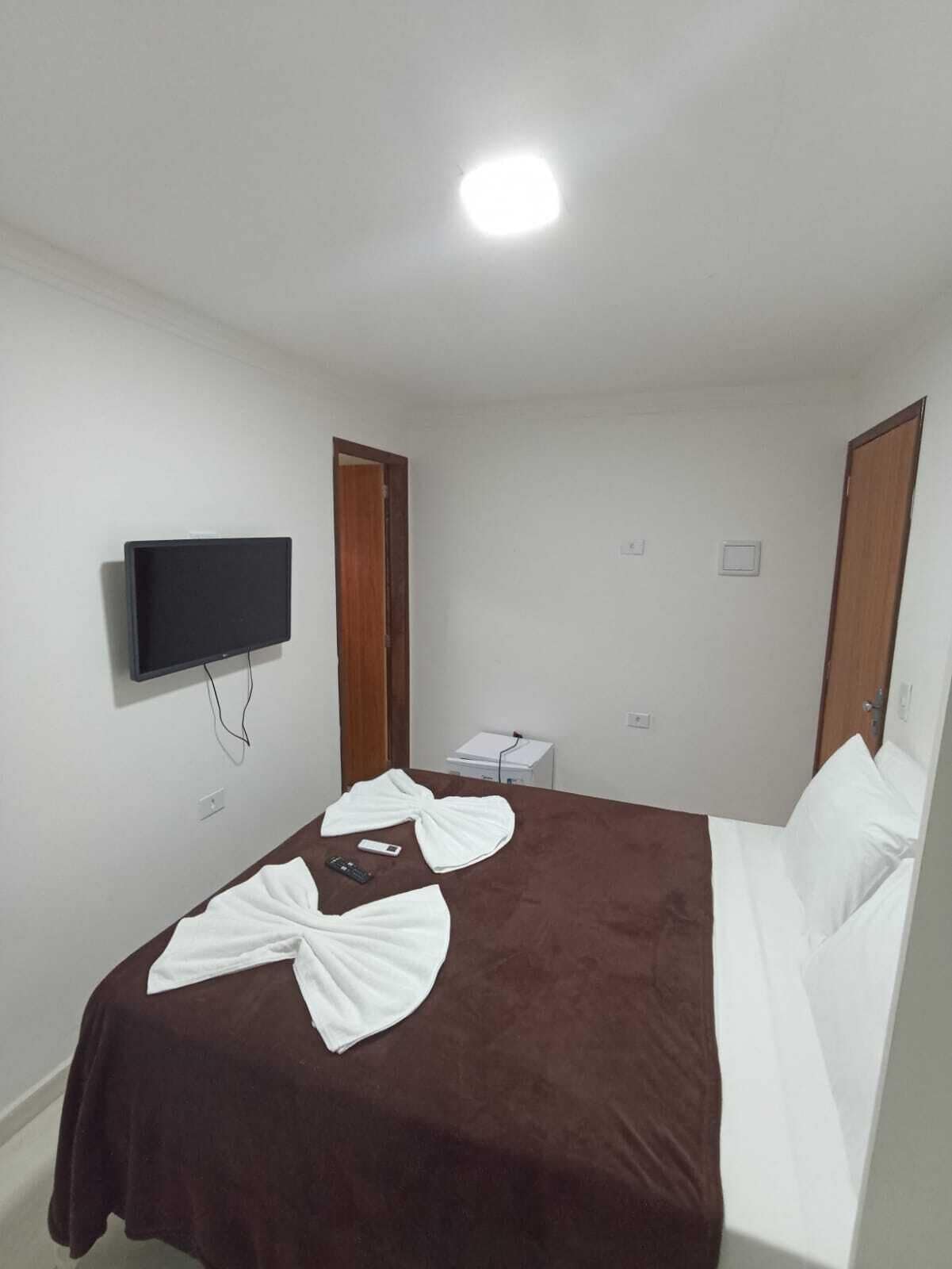 Quarto de hotel com cama, televisão presa na parede, escrivaninha com cadeira e porta.
