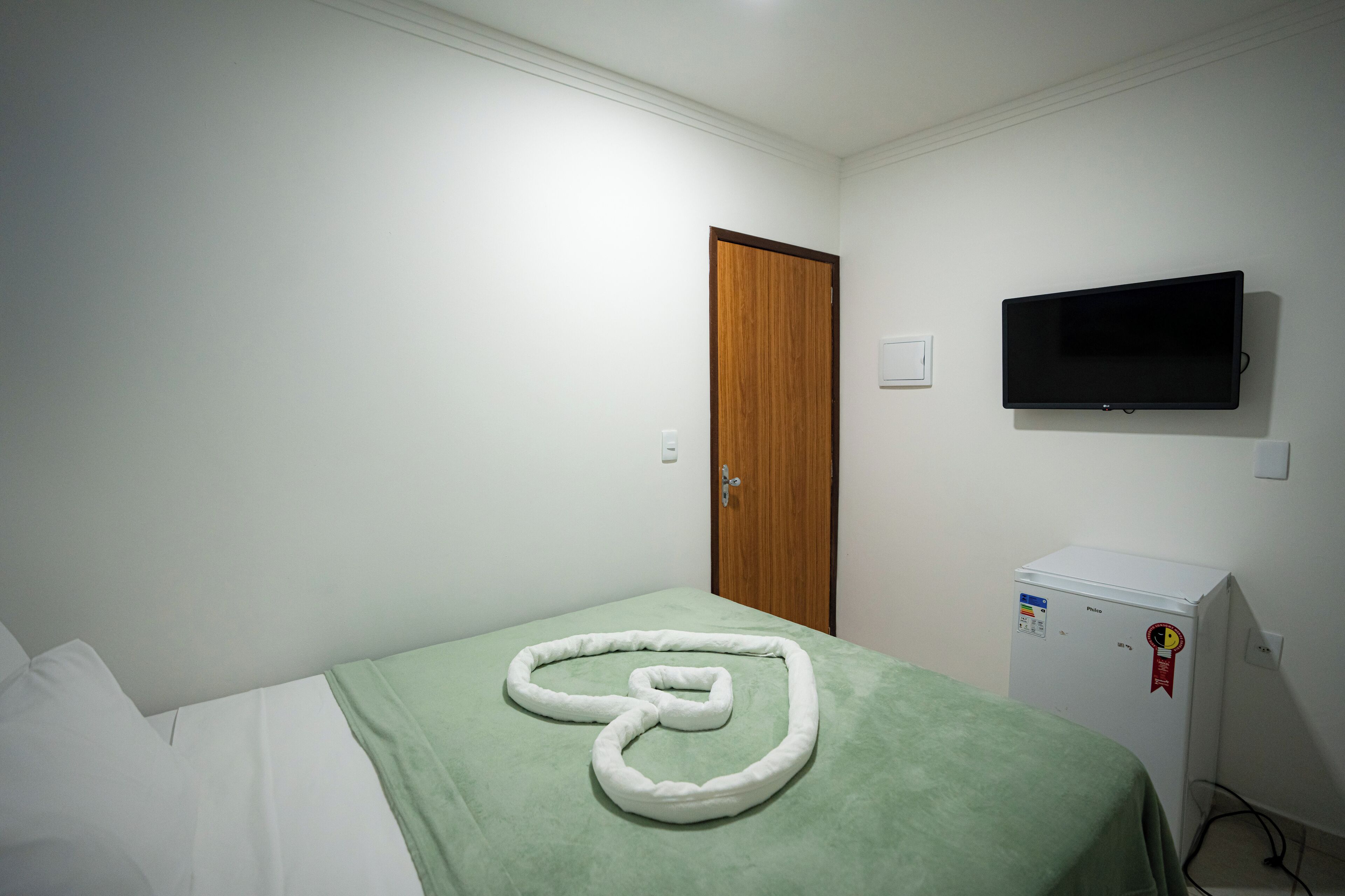 A room with a bed, a television mounted on the wall, and a small refrigerator.