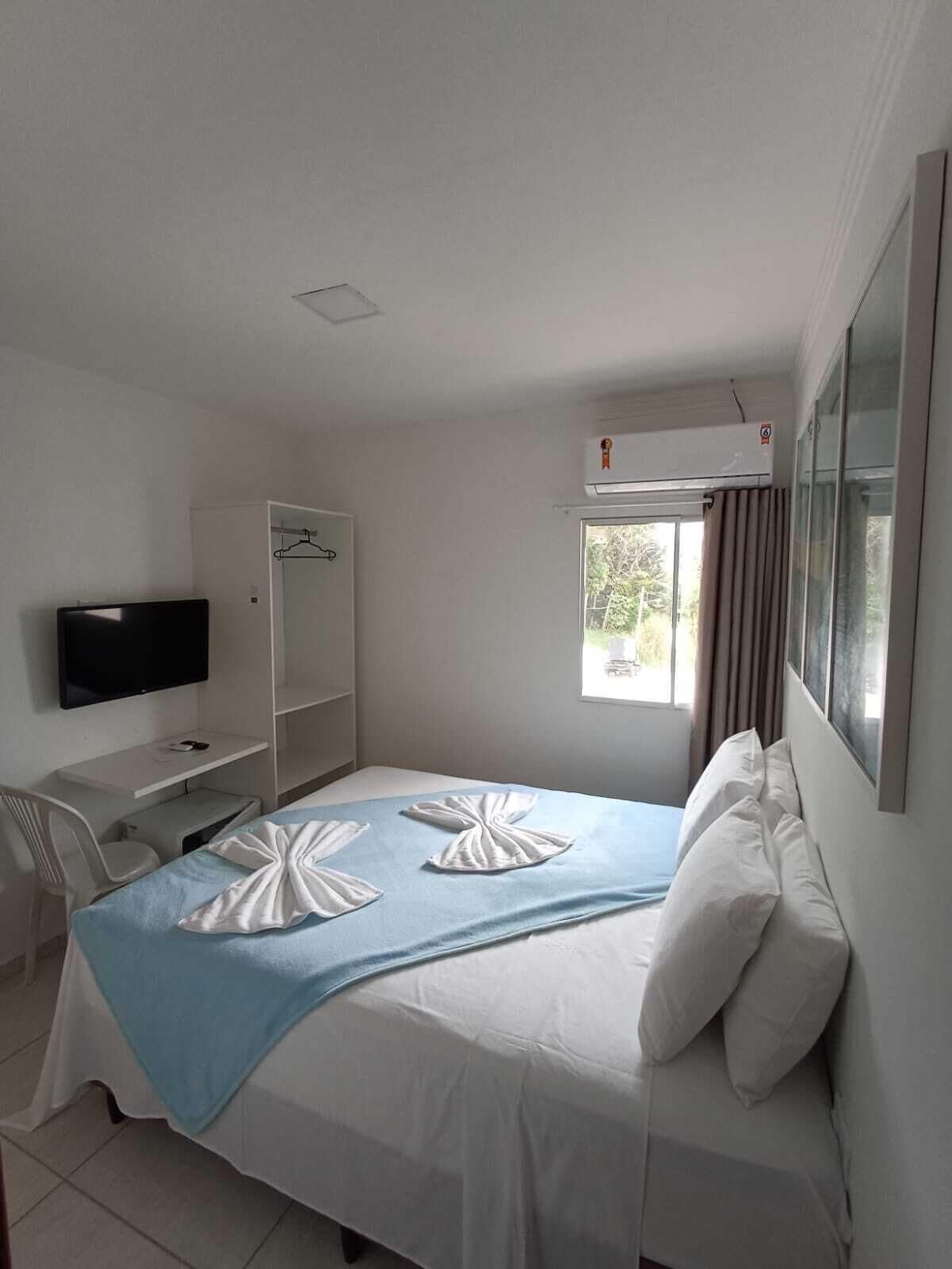 A hotel room with a bed, a TV, a desk, and a window.