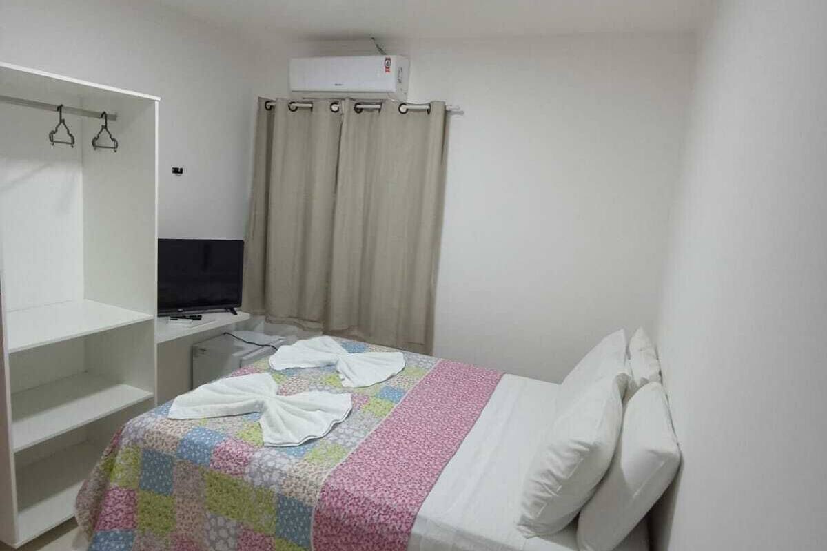A bedroom with a bed, a TV, a wardrobe, and an air conditioner.
