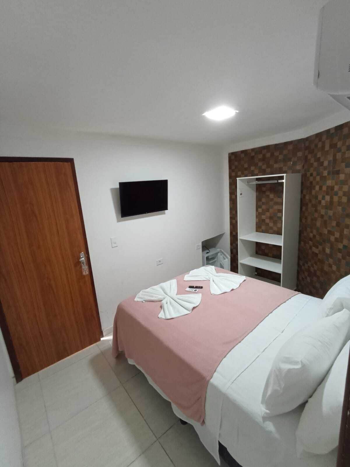 Habitación de hotel con cama, televisión instalada en la pared, armario y suelo de baldosas.