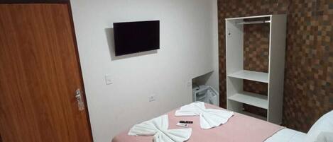 Habitación de hotel con cama, televisión instalada en la pared, armario y suelo de baldosas.