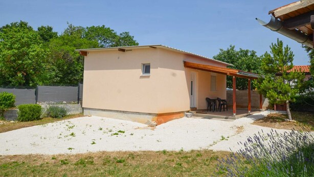 A single-story building with a flat roof, a small window, and a covered patio area with chairs.
