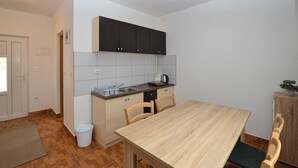 A compact kitchen with a wooden table, two chairs, a sink, and dark cabinets.