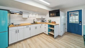 Una cocina moderna con armarios blancos, encimera de madera, microondas y un refrigerador color turquesa.
