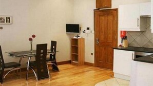 Una cocina moderna con armarios blancos, una puerta de madera y un comedor con mesa y sillas de vidrio.