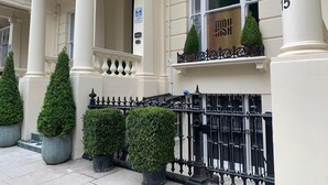 Un edificio con columnas blancas, una verja de hierro forjado y plantas topiarias en macetas.