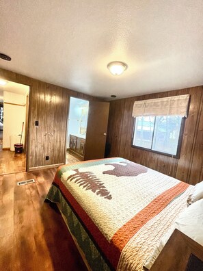 Een slaapkamer met een groot bed, houten wanden, een raam met uitzicht en een deur naar een andere kamer.